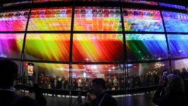 an-image-of-an-array-of-15-transparent-tvs-shot-with-a-fish-eye-lens-and-displaying-colored-squares-with-a-crowd-of-people-vis.jpeg