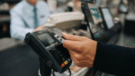 A_closeup_of_a_hand_holding_a_credit_card_up_to_a_credit_card_scanner.png
