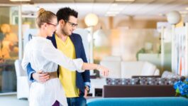 Young couple selecting together sofa in furniture store to furnish home