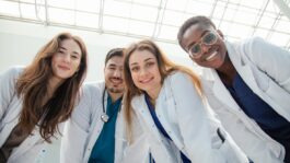 A group of four medical university students in white coats look down and smile A group of four medical university students in white coats look down and smile